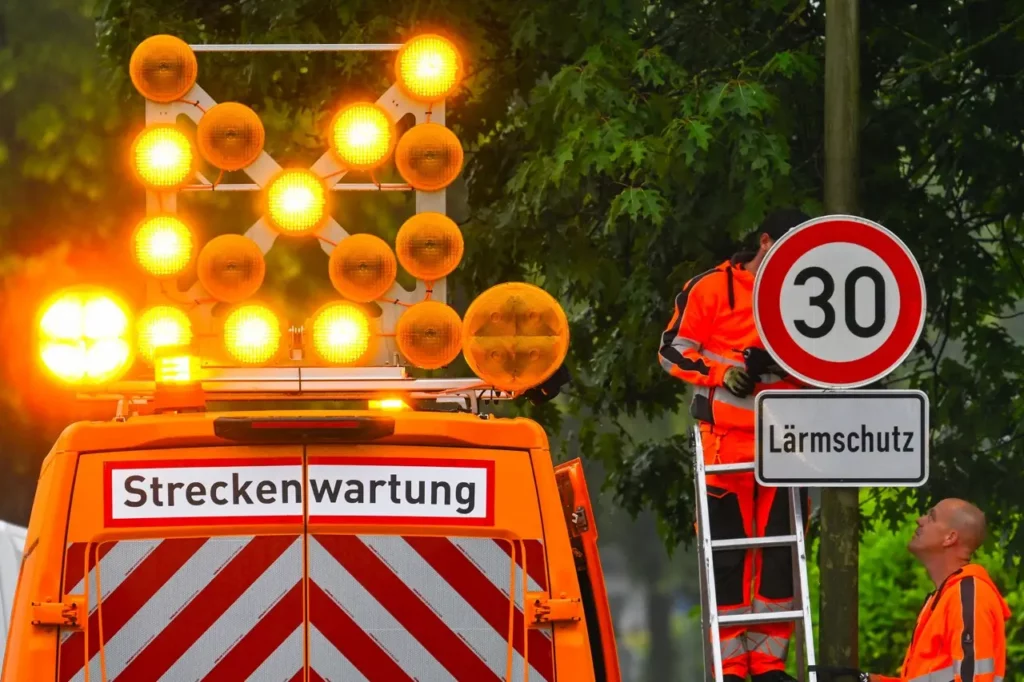 Zwei Arbeiter hängen ein Tempo 30 Schild wegen Lärmschutz auf.